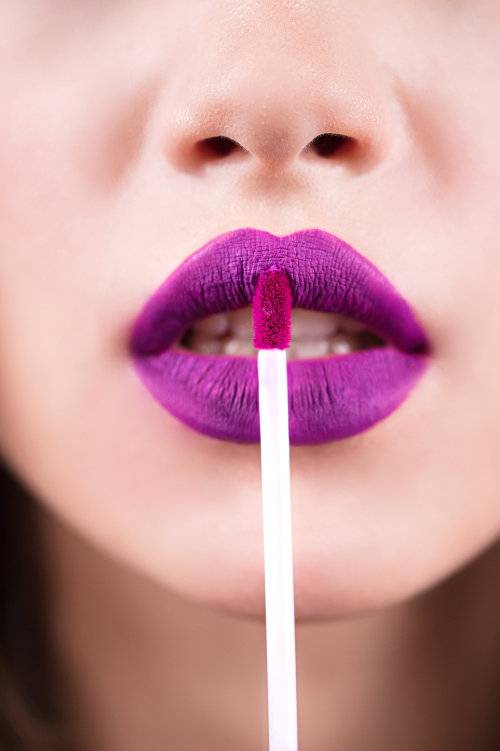 boca feminina utilizando batom roxo com um pincel